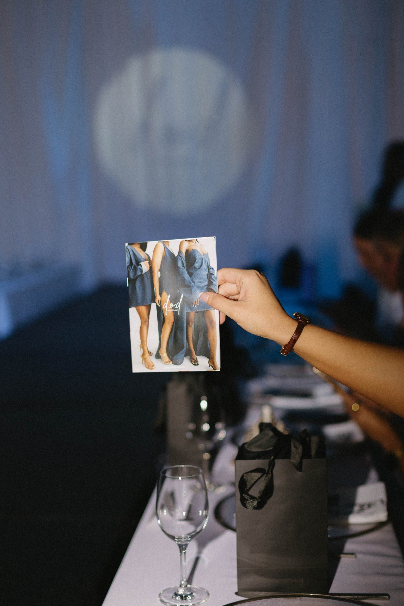 A guest holds the d.o.d lookbook card against the blue-lit runway