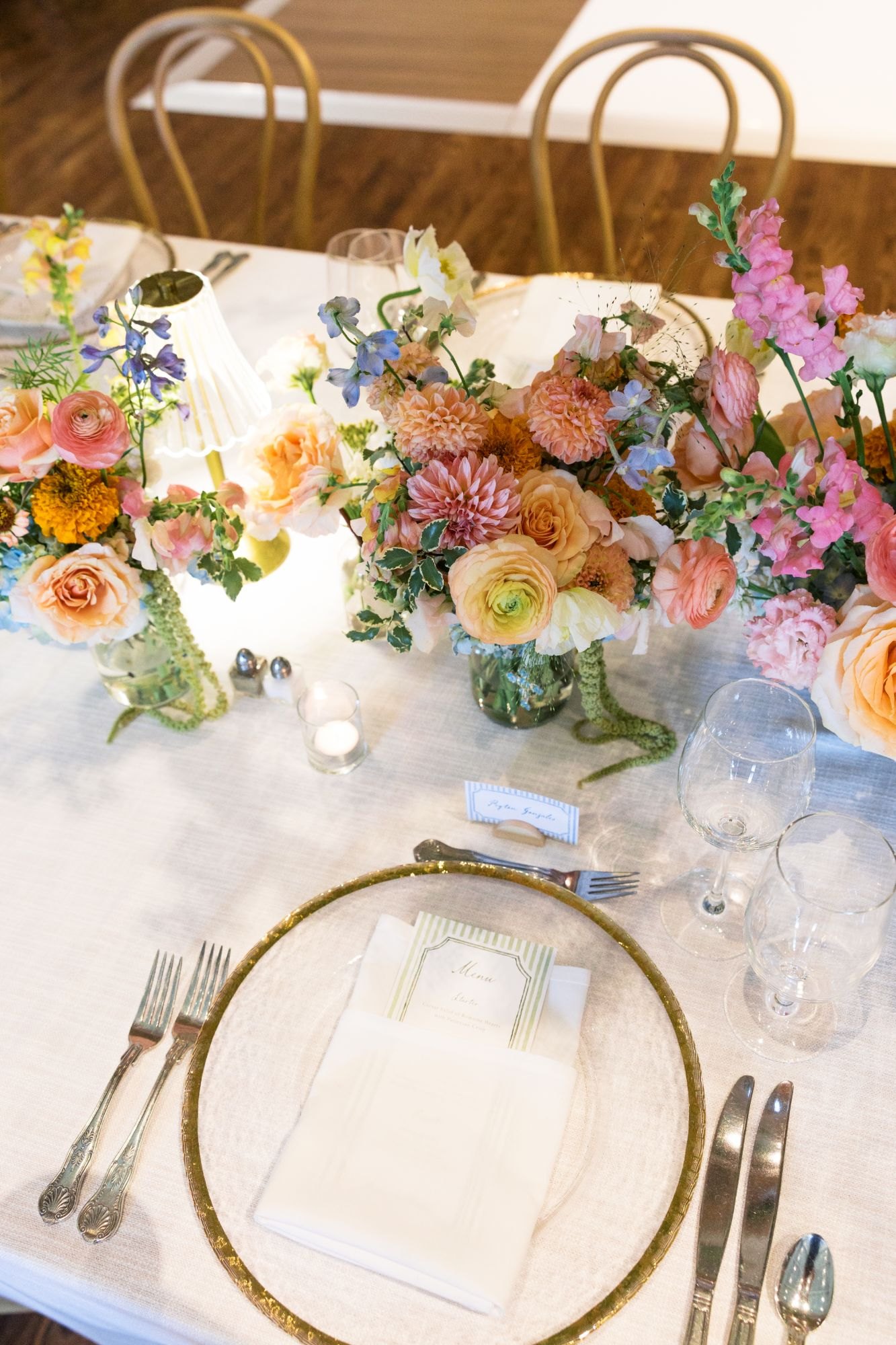 Tablescape detail with gold-rimmed charger, striped menu card and pastel centerpieces