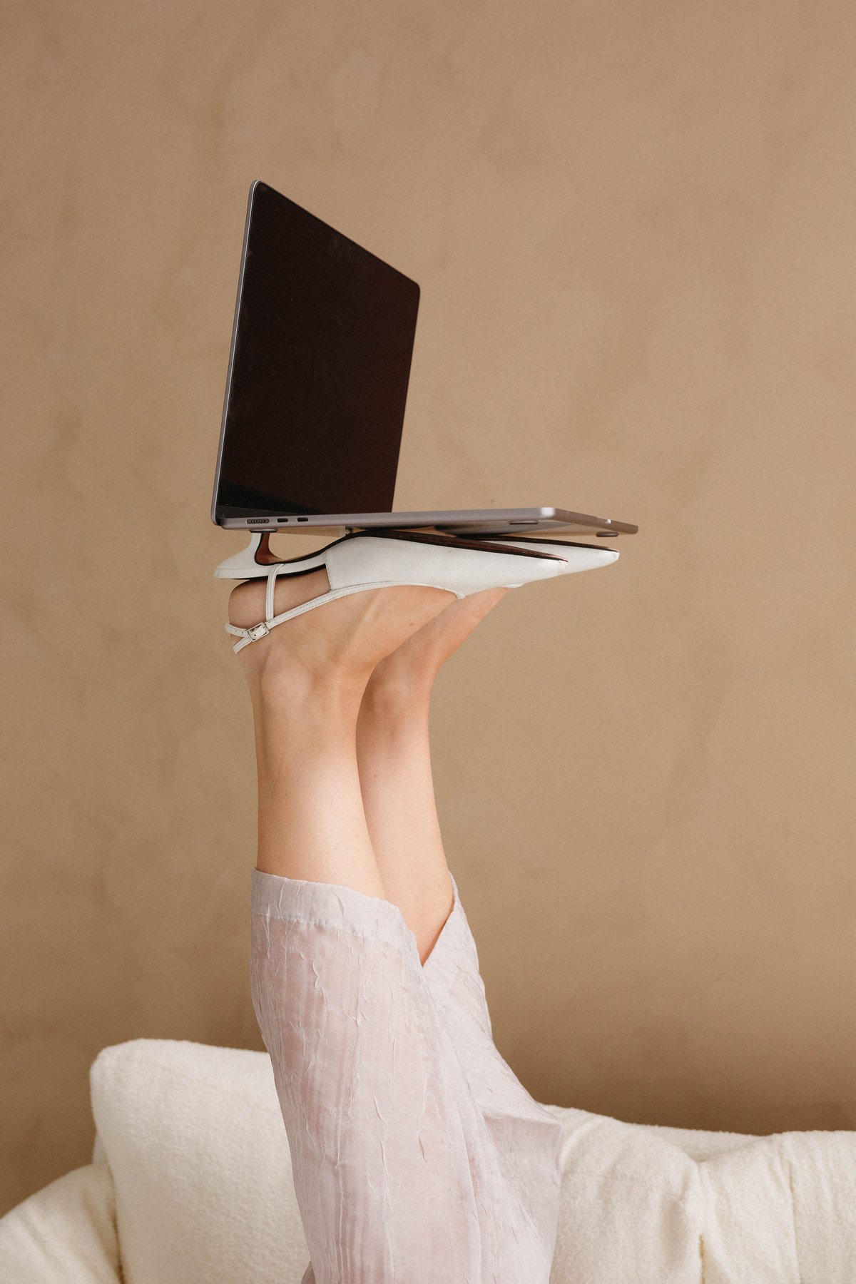 Legs up in white heels balancing an open laptop, an editorial brand moment
