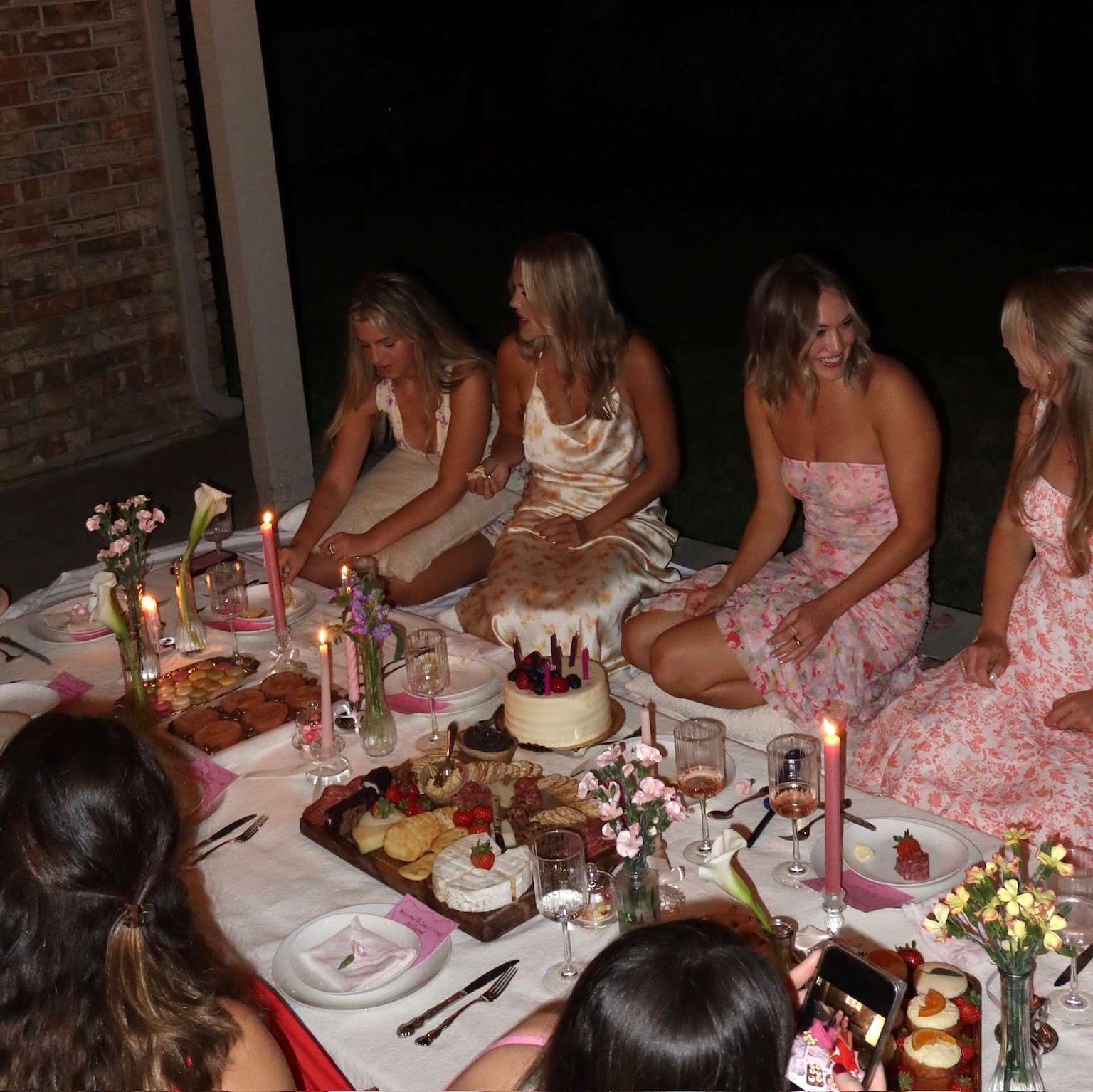Guests in florals gather around the candlelit picnic table