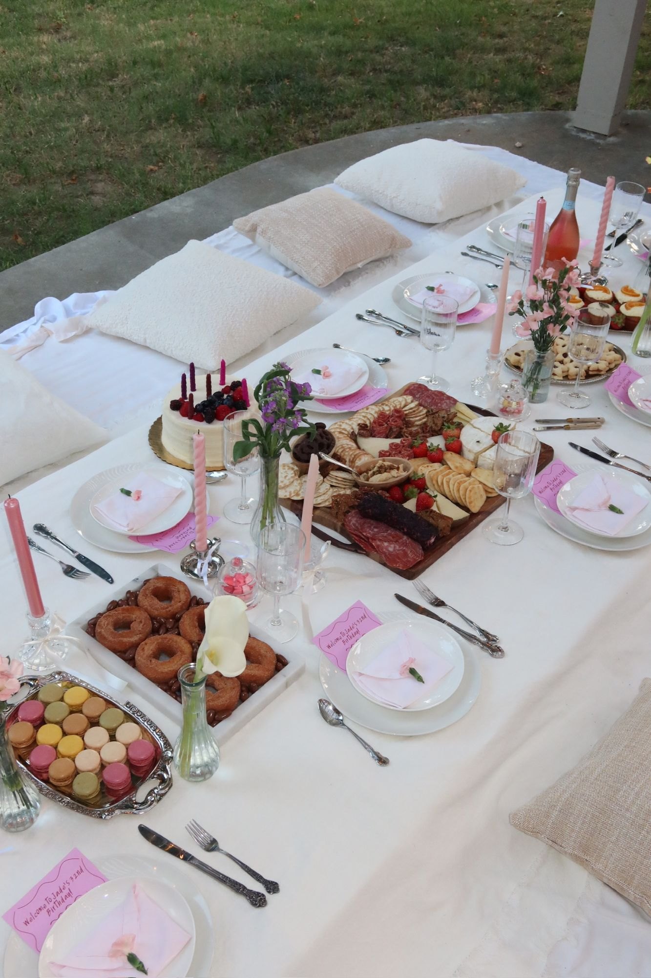 A low picnic table with pillow seating, charcuterie board, macarons and pink details