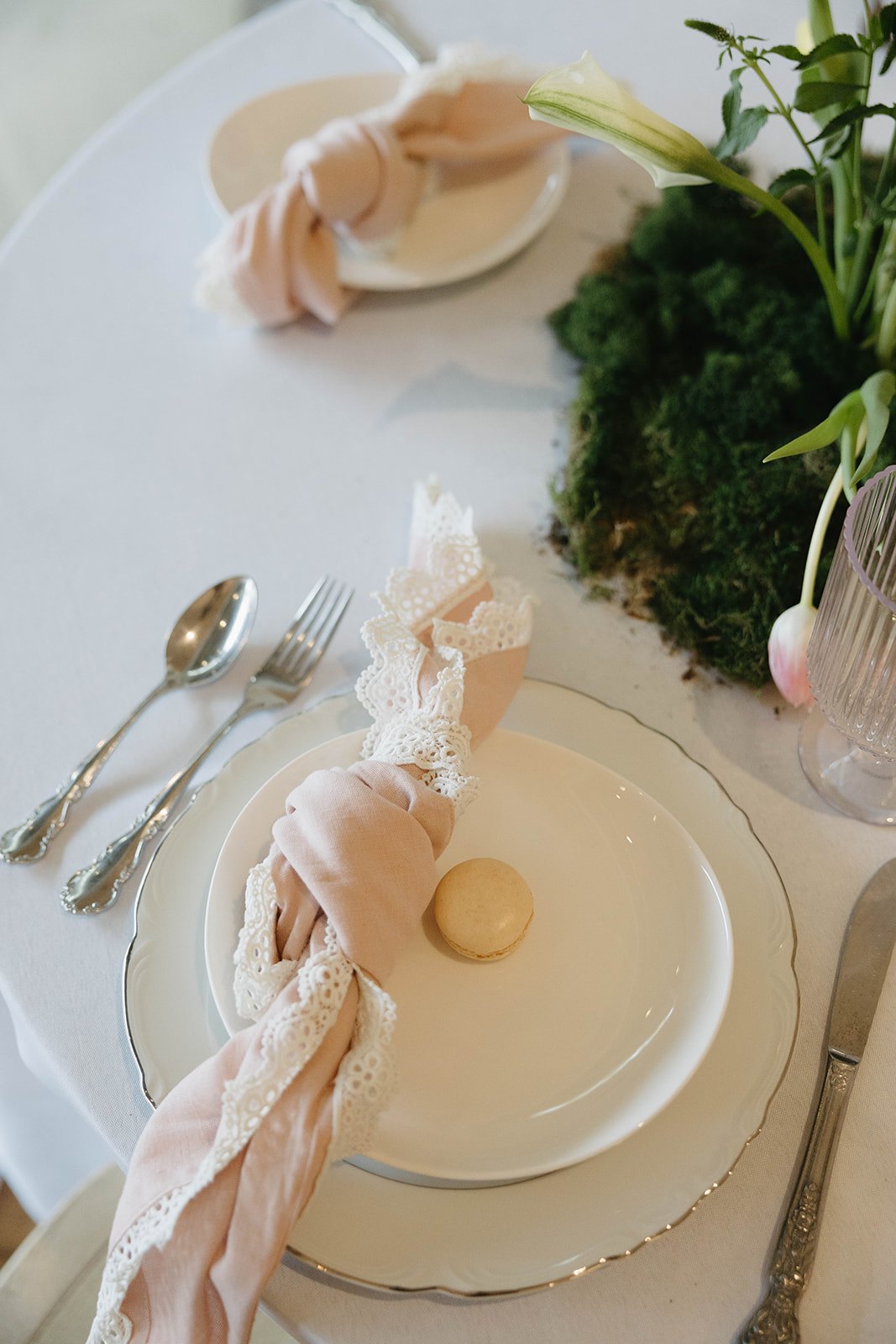 A blush napkin knotted with lace beside the moss centerpiece