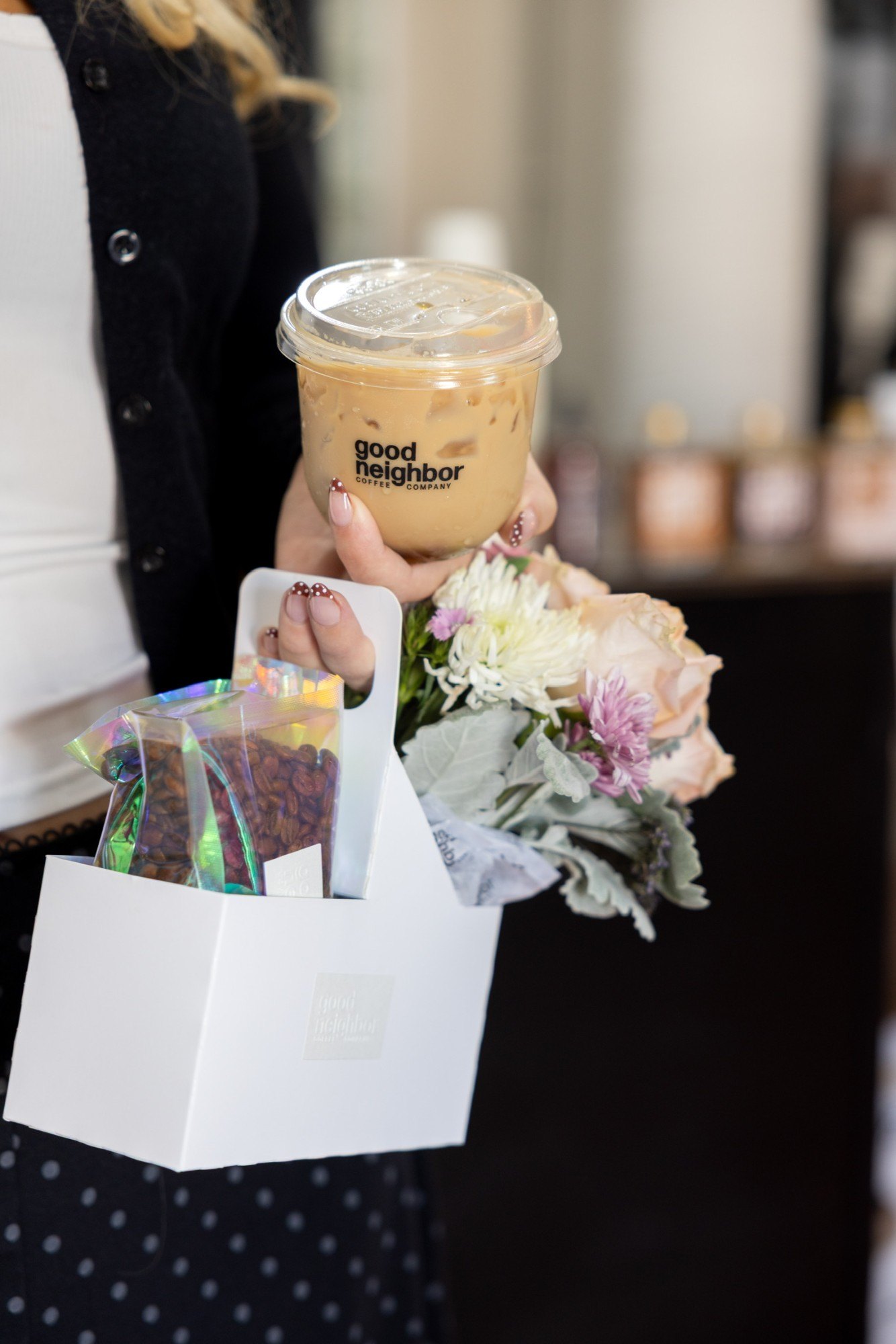 An iced Good Neighbor coffee held over a gift box of beans and flowers
