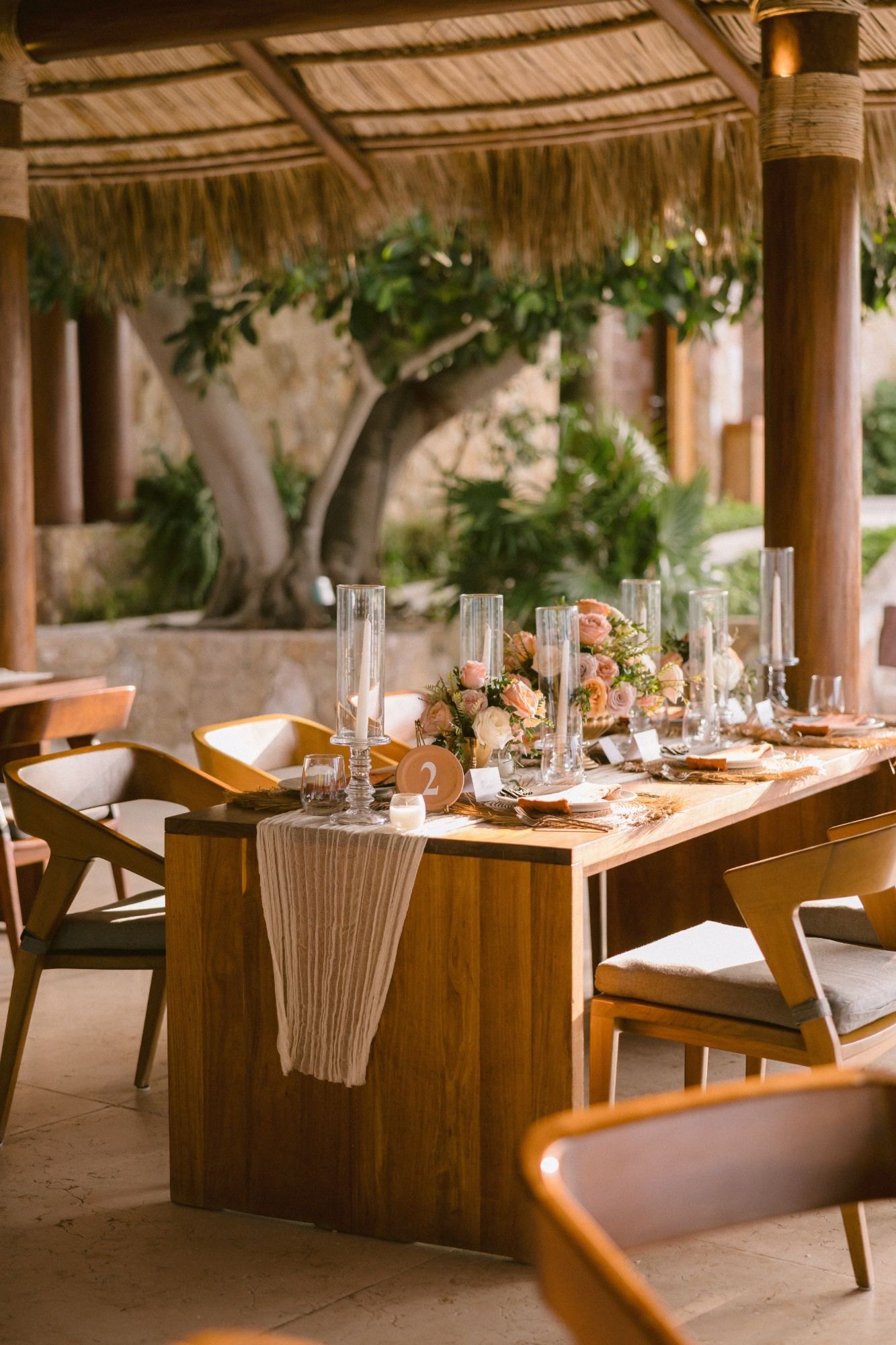 A wooden reception table set under the palapa with candles and blush florals