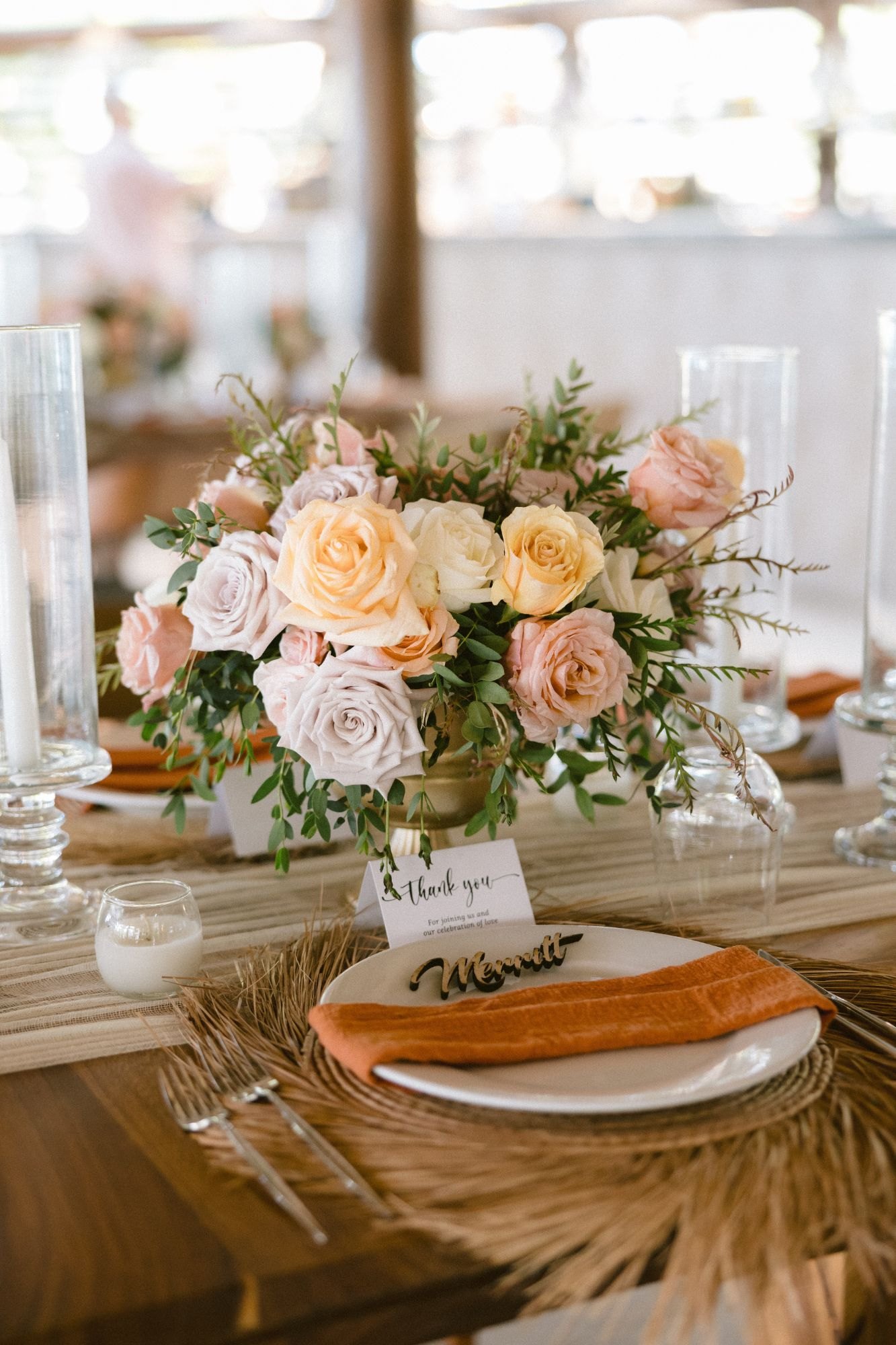 A peach and blush rose centerpiece over a woven place setting with terracotta napkin