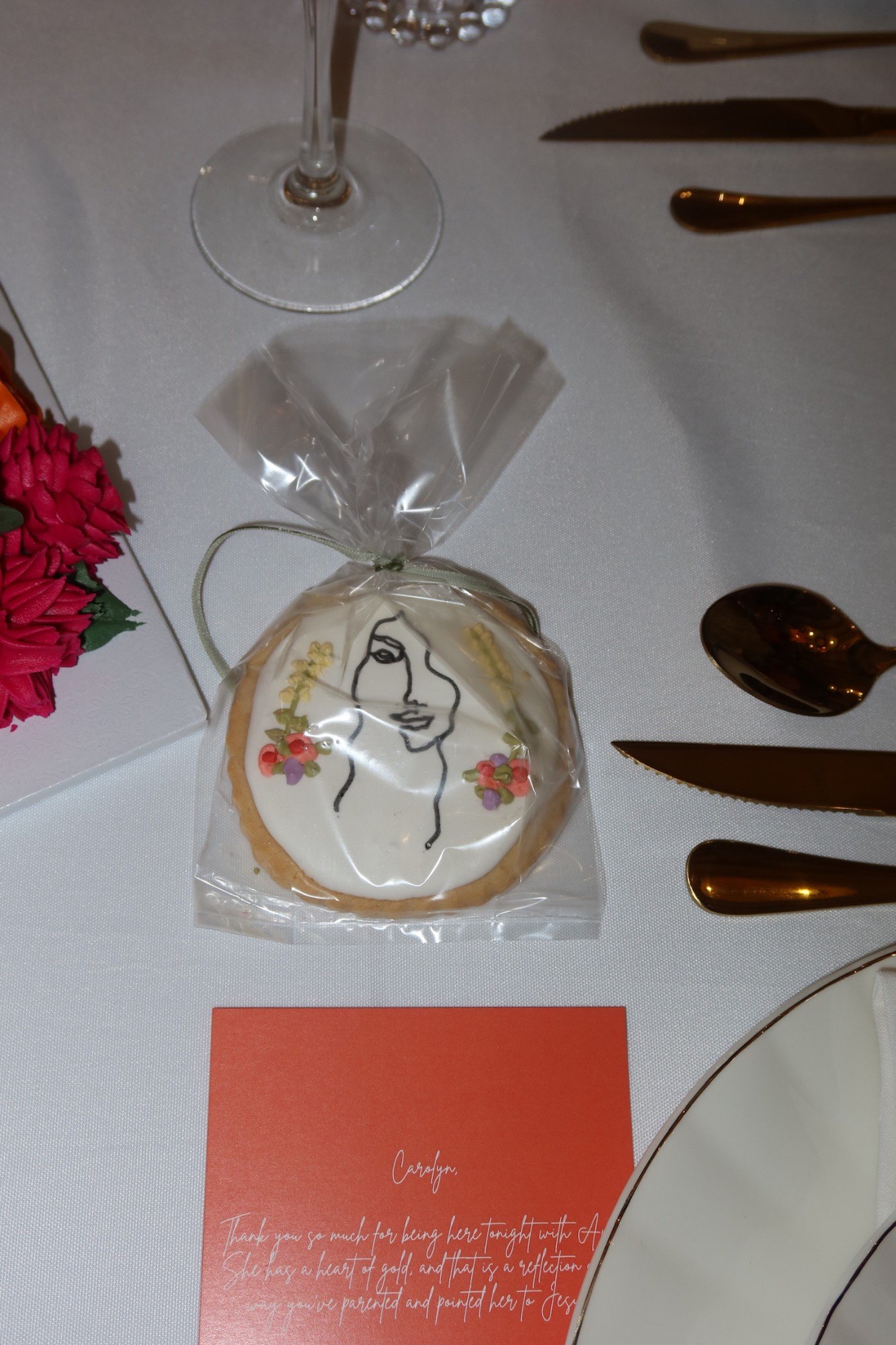 An iced line-art cookie favor tied with ribbon over a personalized note