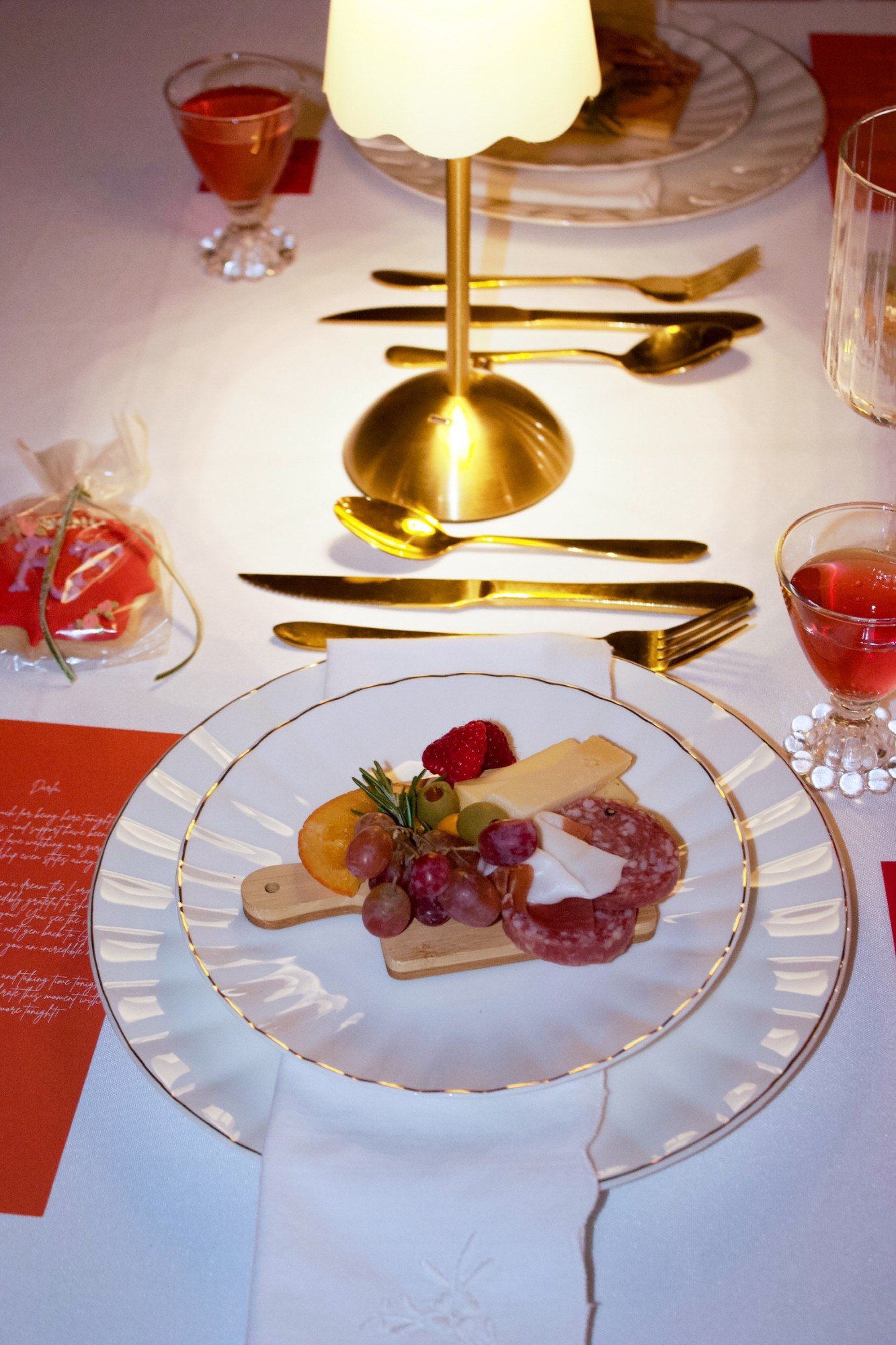 A place setting with a mini charcuterie board, gold flatware and a glowing lamp