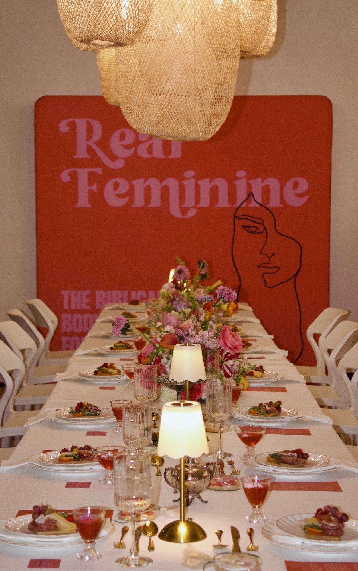 The long table with pink florals and lamps leading to the Real Feminine backdrop