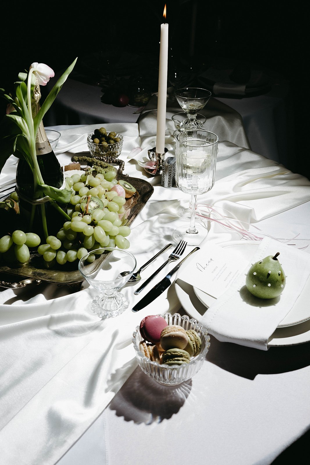 Grapes, macarons and a taper candle over white satin by candlelight