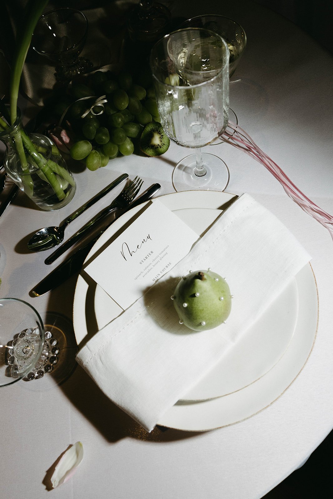 A calligraphed menu and pearl-studded pear on linen from above