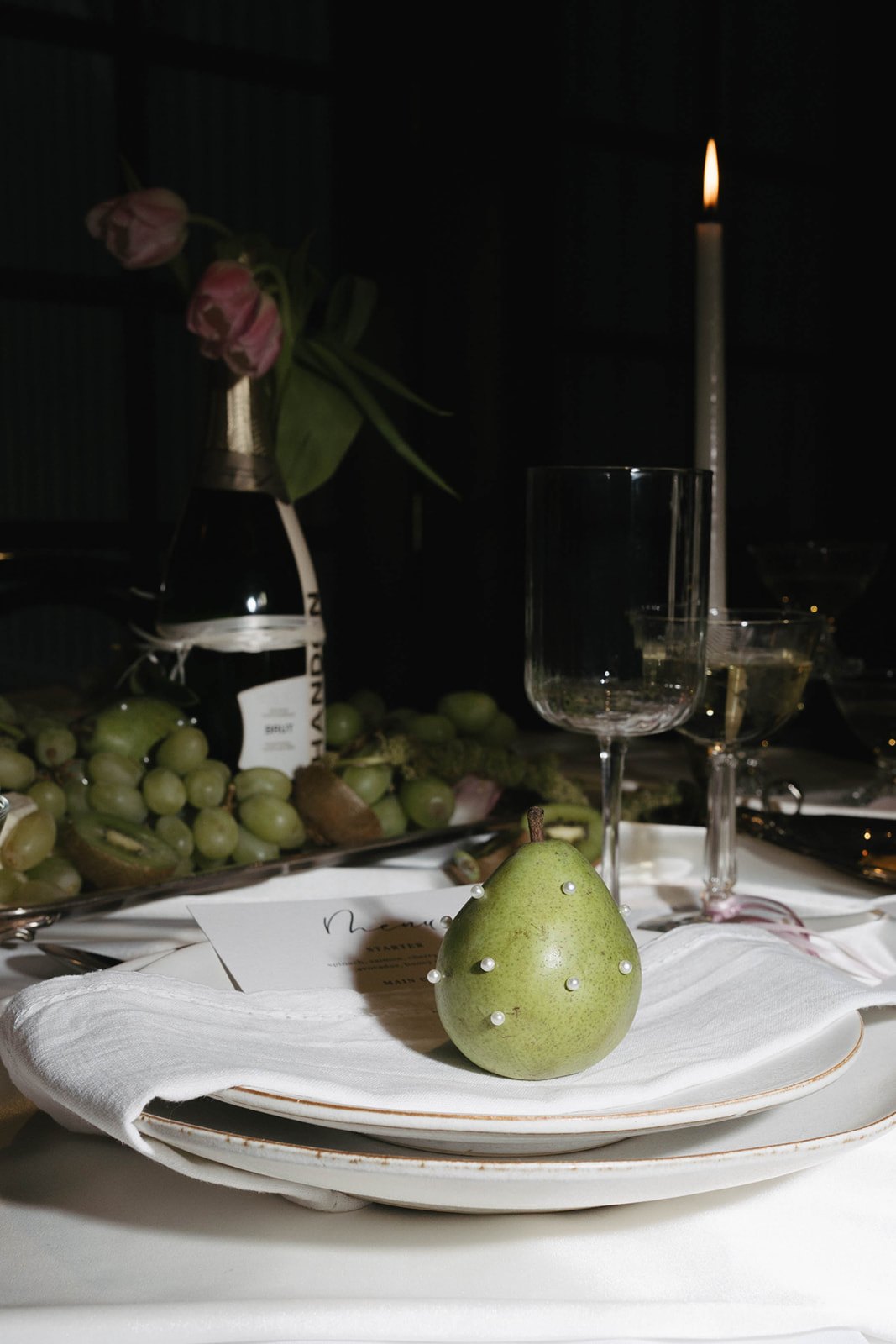 A pearl-studded pear on the place setting beside champagne coupes