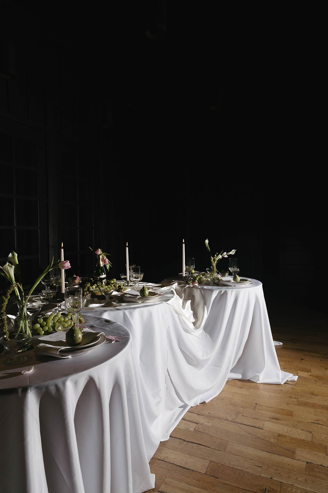 The draped white tables glowing by taper light in the dark room