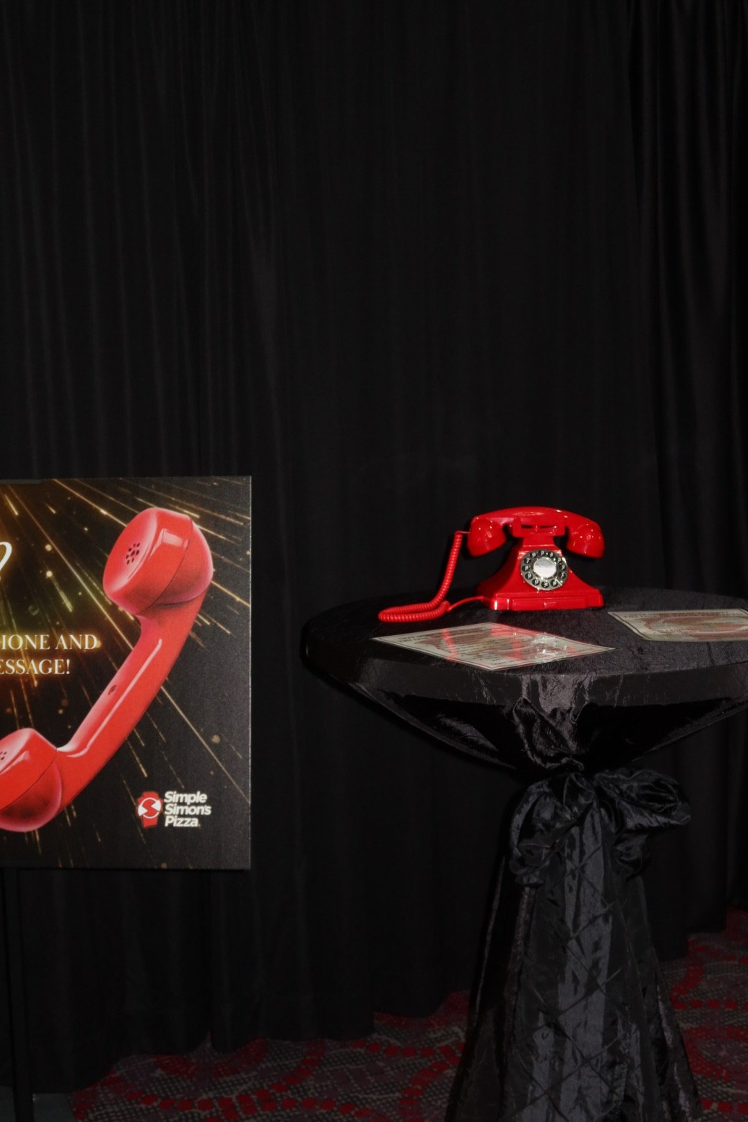 A red rotary phone message station against black drape