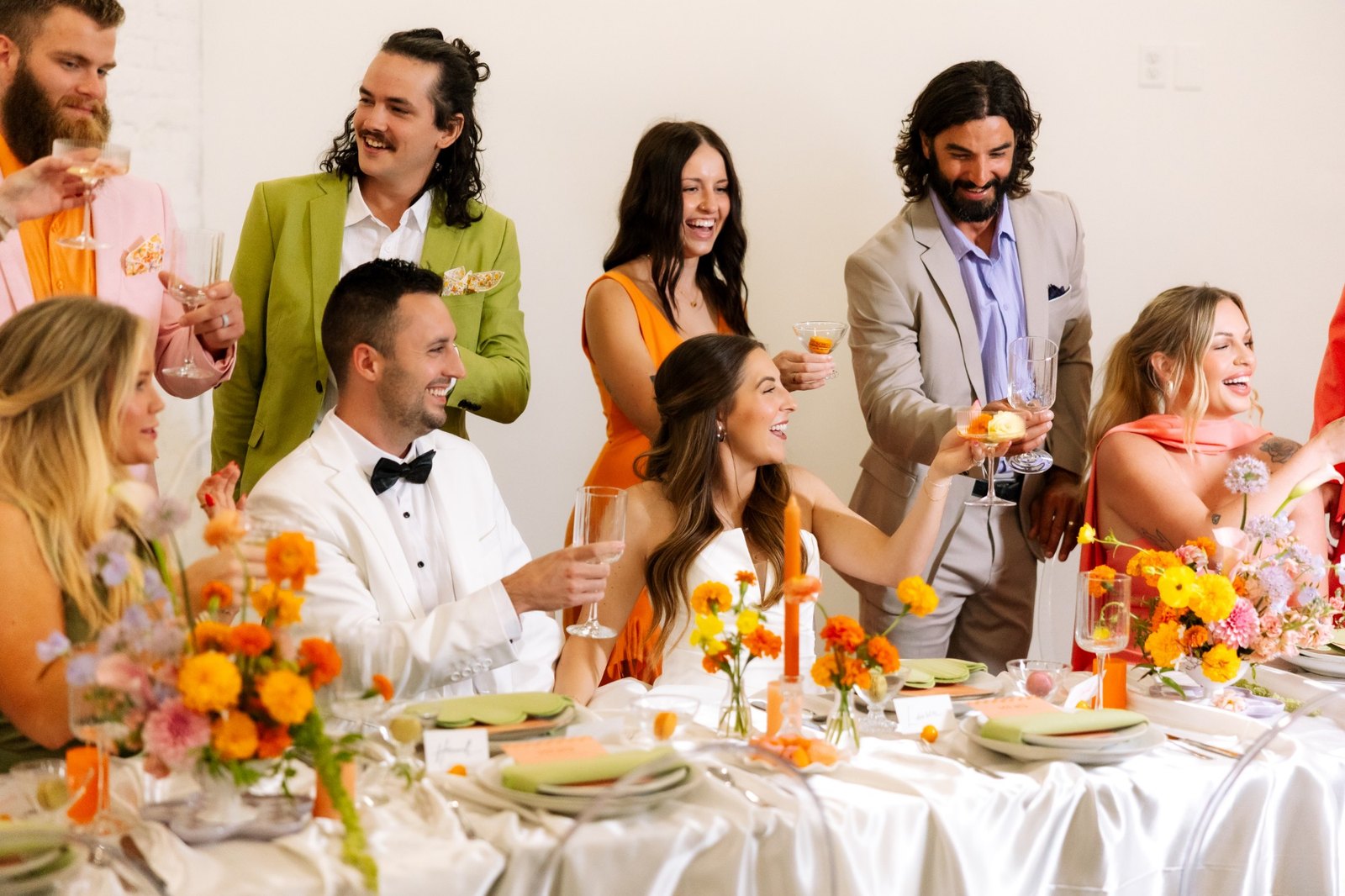 The couple in white toasts as friends in color gather around them