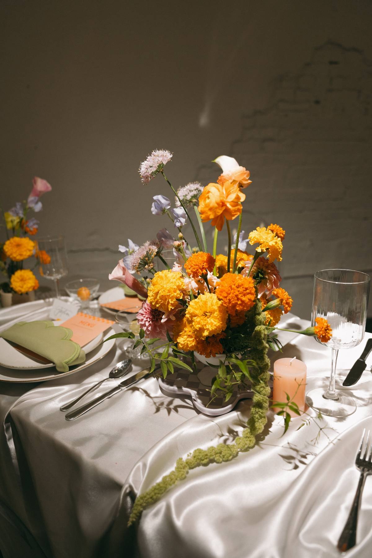 A marigold, dahlia and sweet pea arrangement on satin linen