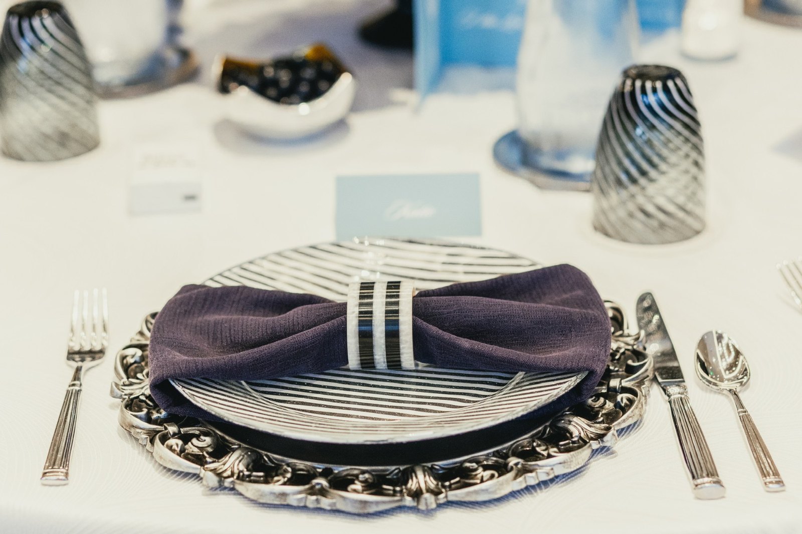 A striped place setting with navy napkin on an ornate silver charger