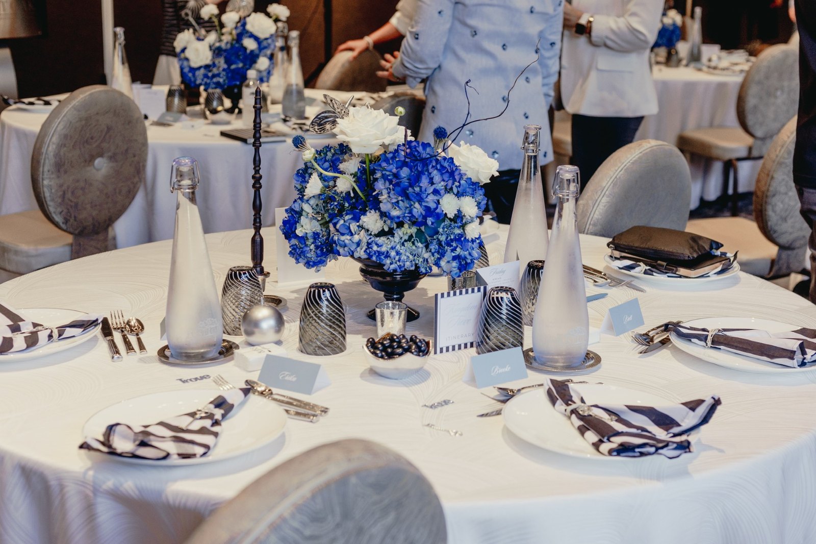 A round table set in blue, white and silver with striped napkins and itineraries